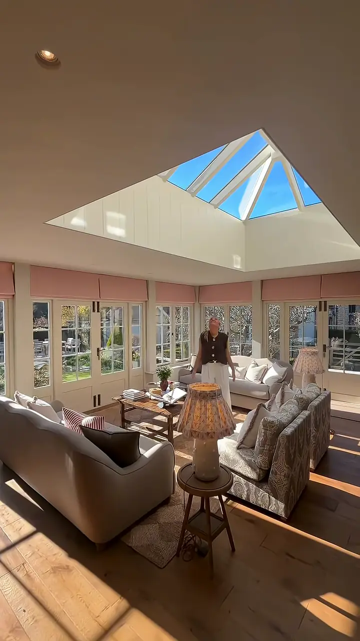 A bright garden room with a glass roof, sofas and a long table.