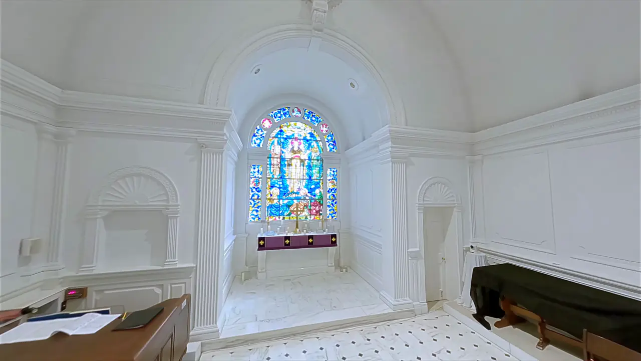 A white chancel with a tall stained-glass window of Christ.
